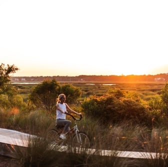 Woman biking on boardwalk with sunset 