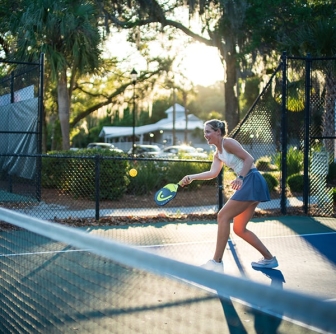 woman playing pickleball at Palmetto Dunes Pickleball Center with sun shining between trees