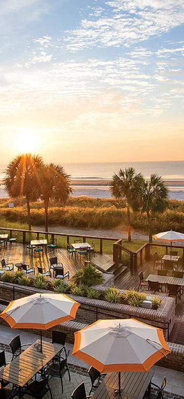 view of the beach from a balcony at sunset overlooking patios with umbrellas