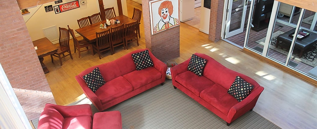A living room and dining area with two red couches and two wood dining tables. 